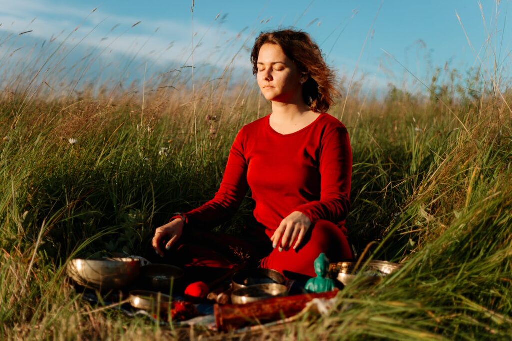 a-woman-in-red-long-sleeve-dress-meditating-on-grass-field-5416014