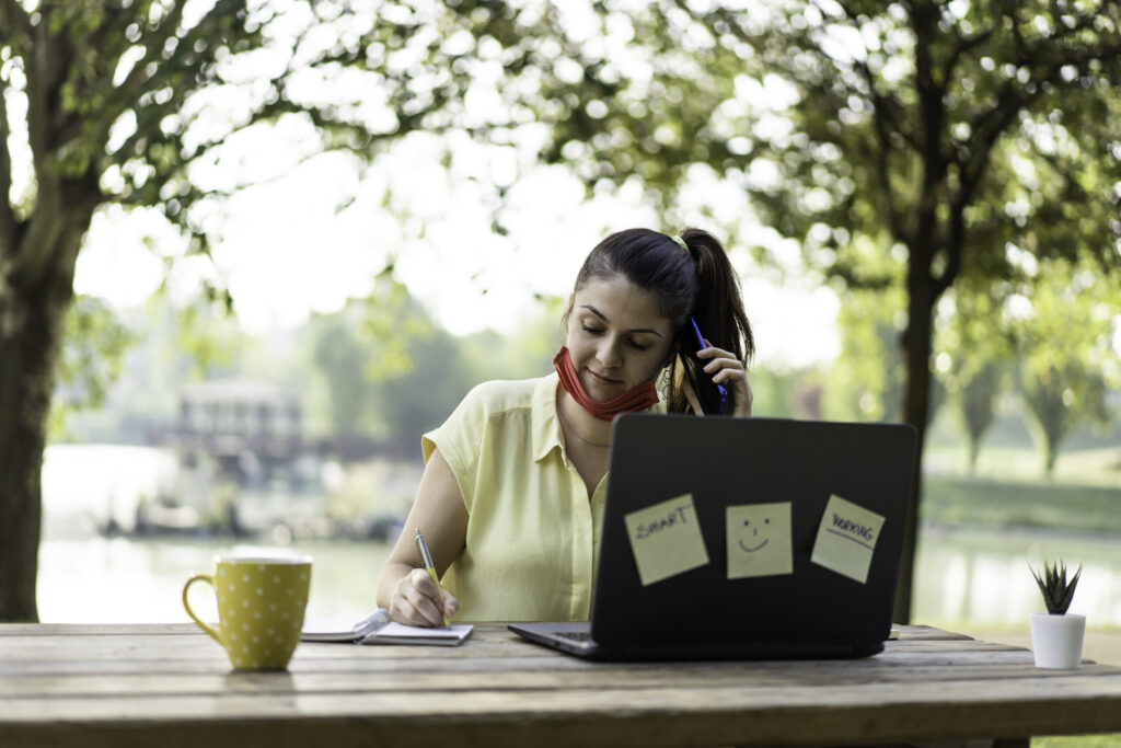 smiling-businesswoman-wearing-mask-working-cafe-scaled